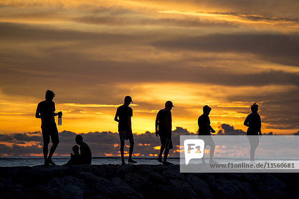 Indonesien  Bali  Menschen bei Sonnenuntergang an der Meeresküste