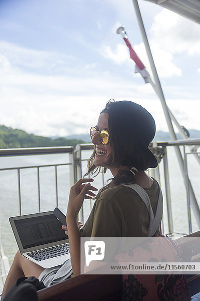 Indonesien  Insel Lombok  glückliche Frau mit Laptop auf dem Schiffsdeck