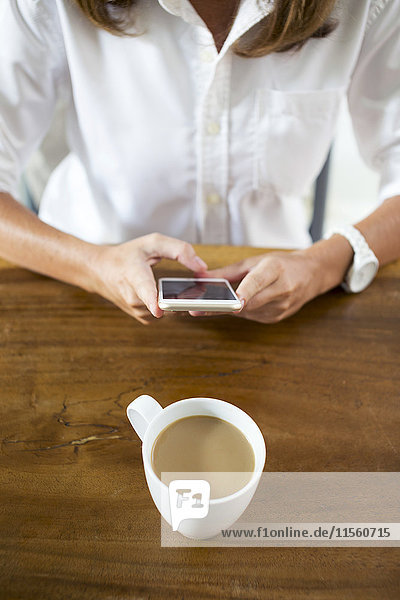 Frau mit Tasse Kaffee am Tisch per Handy