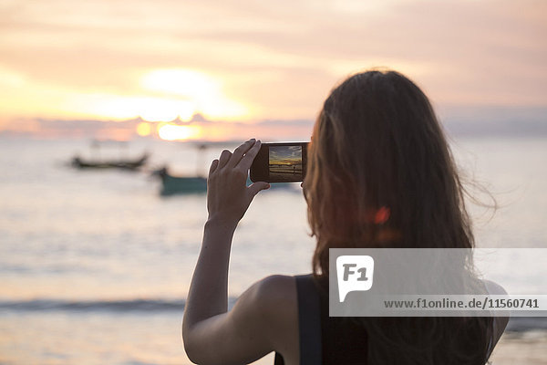 Indonesia  Bali  woman taking a picture of the sunset over the ocean