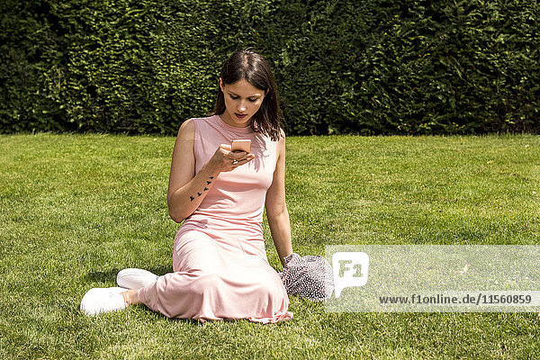Junge Frau sitzt auf einer Wiese und schaut aufs Handy.