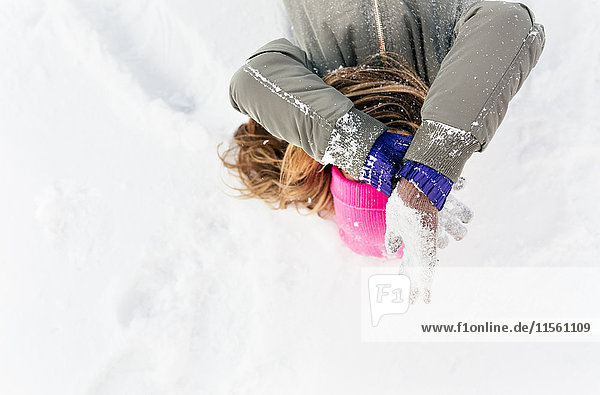 Junge Frau liegt im Schnee und bedeckt ihr Gesicht.