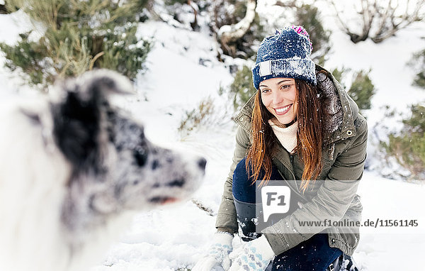 Schöne Frau  die mit ihrem Hund im Schnee spielt.