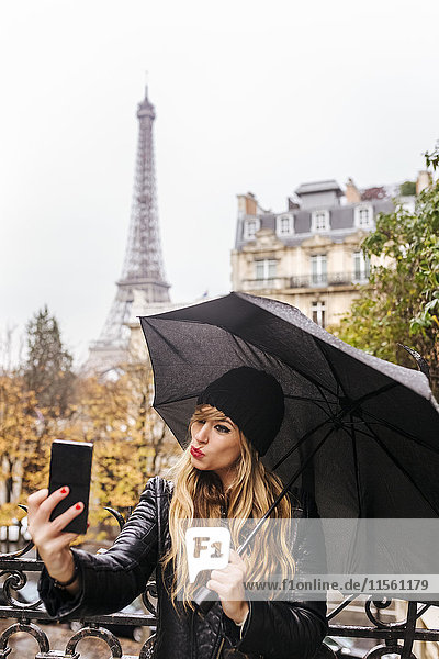 Frankreich  Paris  junge Frau  die einen Selfie mit dem Eiffelturm im Hintergrund nimmt.