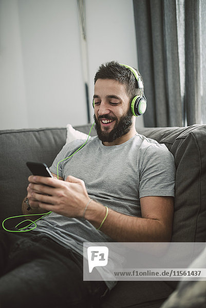 Young man sitting on sofa  listening music from his smart phone
