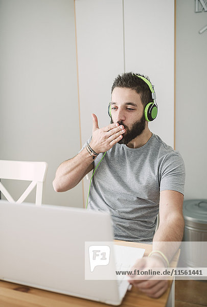 Young man wearing headphones  using laptop and blowing a kiss