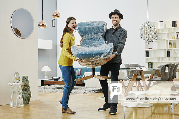 Happy couple carrying new arm chair out of furniture store