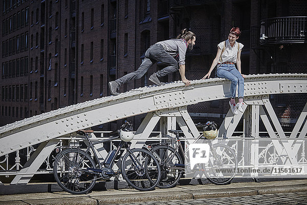 Deutschland  Hamburg  Paar mit Elektrofahrrädern  die Spaß auf einer Brücke haben