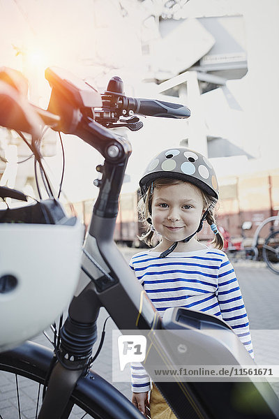 Portrait of smiling girl wearing helmet next to bicycle