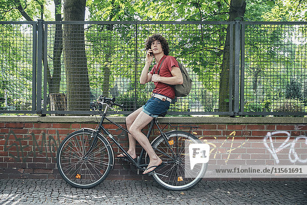 Junger Mann am Telefon auf dem Fahrrad sitzend
