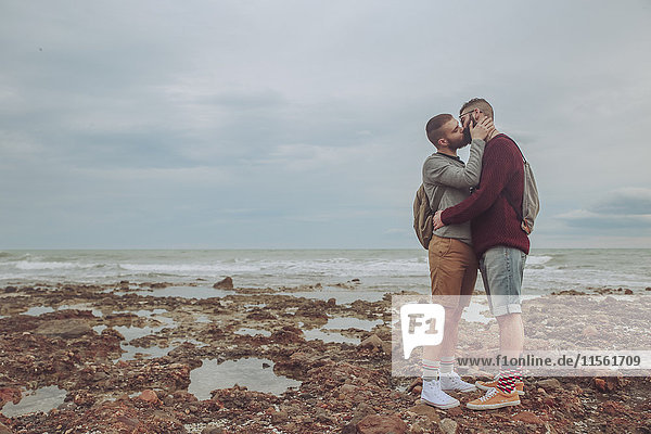 Junges schwules Paar beim Küssen am Strand