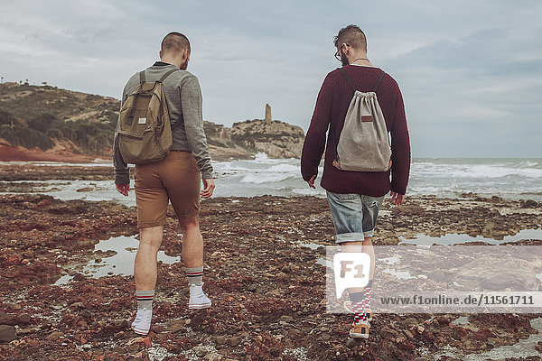 Spanien  Oropesa del Mar  zwei junge Männer  die am steinigen Strand spazieren gehen