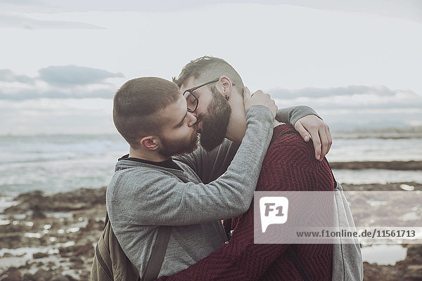 Junges schwules Paar  das sich vor dem Meer umarmt und küsst.