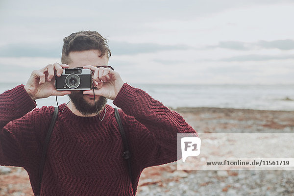 Bearded man taking photo on the beach with vintage camera
