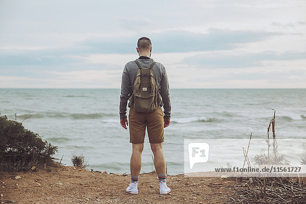 Back view of young man with backpack looking to the sea