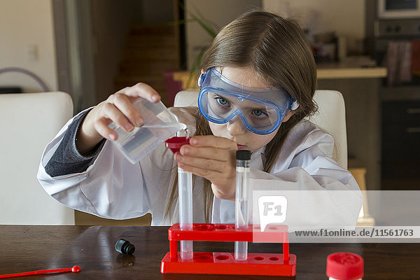 Mädchen in Arbeitsmantel und Schutzbrille mit Chemie-Set zu Hause