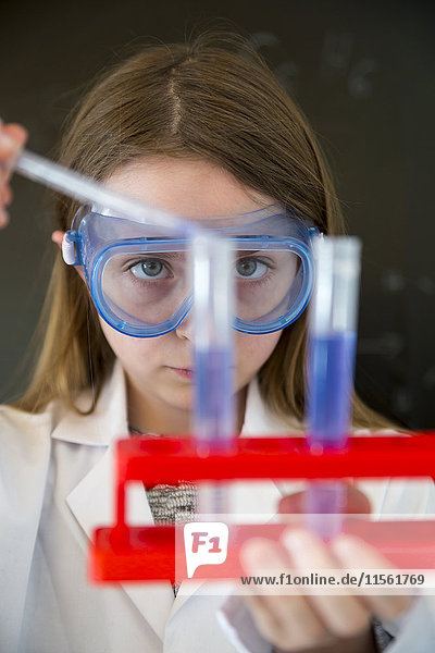 Porträt eines Mädchens mit Arbeitsmantel und Schutzbrille beim chemischen Experiment