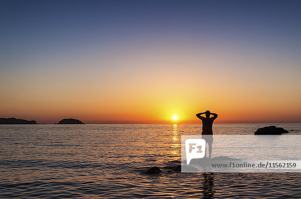 Spain  Menorca  Playa de Cavalleria  man on rock in the sea at sunset