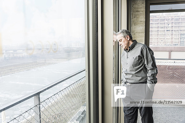 Exhausted senior businessman leaning against window