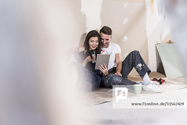 Junges Paar auf der Baustelle seines neuen Zuhauses mit Hilfe eines digitalen Tabletts
