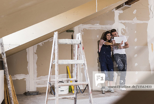 Junges Paar auf der Baustelle seines neuen Zuhauses mit Hilfe eines digitalen Tabletts