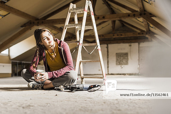 Unabhängige junge Frau renoviert ihr neues Zuhause  sitzt auf dem Boden mit einer Tasse Kaffee.