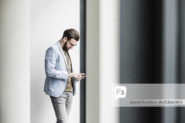 Ein junger Geschäftsmann  der im Büro steht und ein Smartphone benutzt.