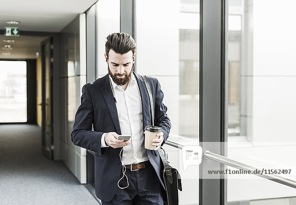 Businessman walking in office building while talking on the phone with ear phones