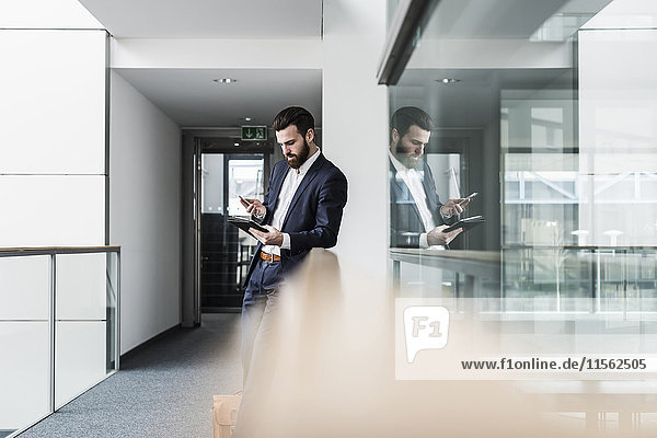 Businessman standing in office building  using smart phone and digital tablet
