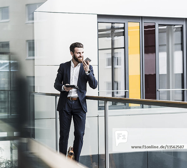 Geschäftsmann im Bürogebäude mit Smartphone und digitalem Tablett