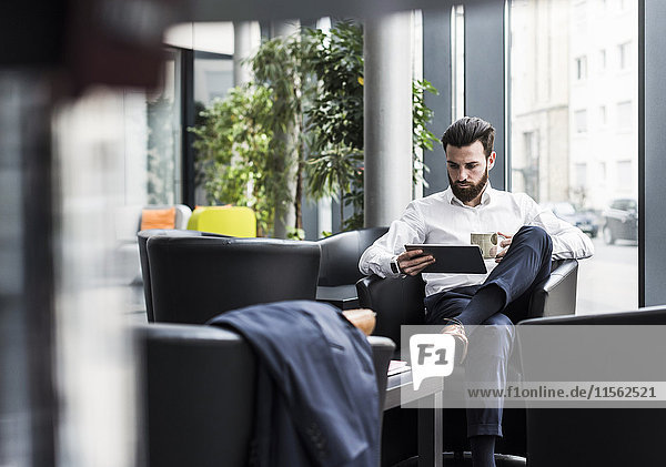 Businessman sitting in lobby  drinking coffee  using laptop