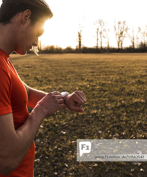 Sportler in ländlicher Landschaft mit Blick auf smartwatch