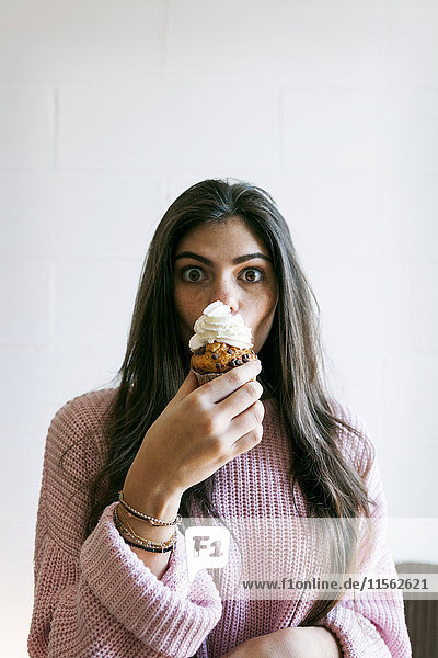 Young woman eating a cup cake with whipped cream