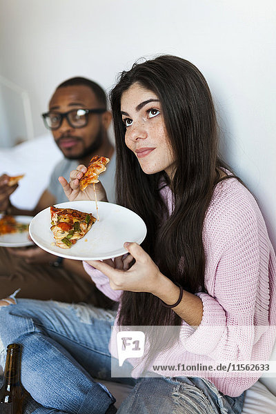 Junges Paar sitzt zu Hause und isst Pizza.