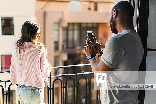Young couple standing on balcony taking smart phone pictures