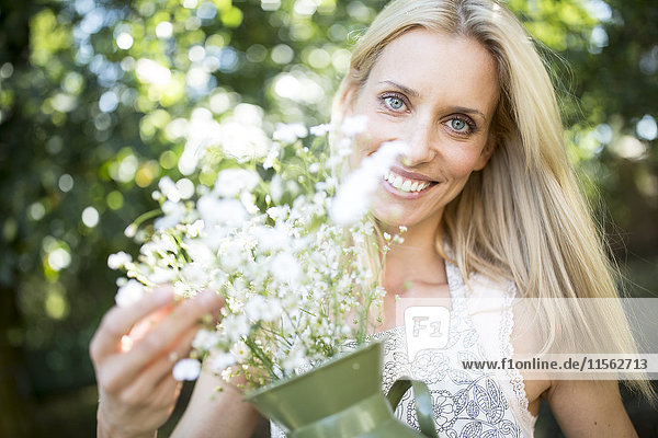 Lächelnde Frau hält Krug mit Blumen im Freien