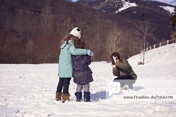Mother taking picture of two children in winter landscape