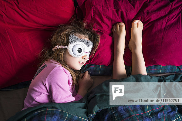 Mädchen mit Schlafmaske und Barfußbeinen einer anderen Person nebeneinander auf dem Bett