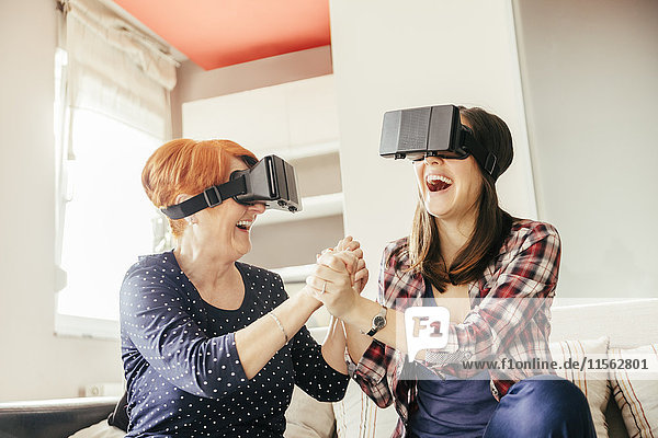 Excited adult daughter with mother at home wearing VR glasses
