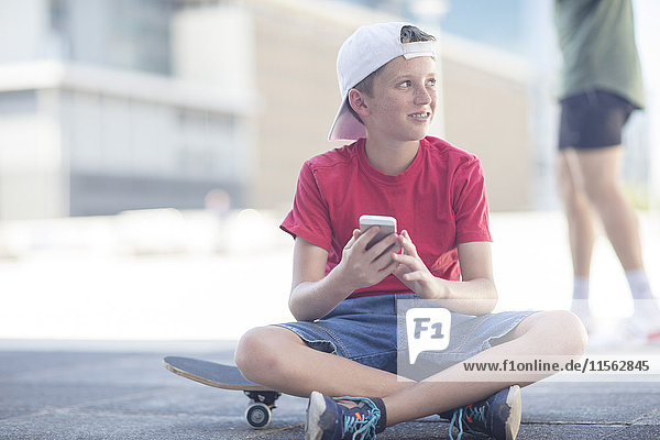 Junge mit Smartphone  sitzend auf Skateboard