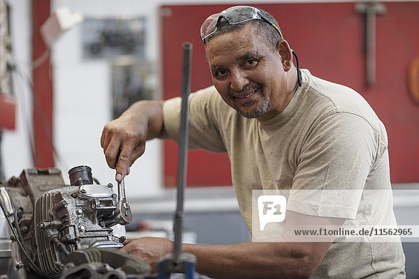 Lächelnder Mechaniker bei der Arbeit am Motorradmotor in der Werkstatt