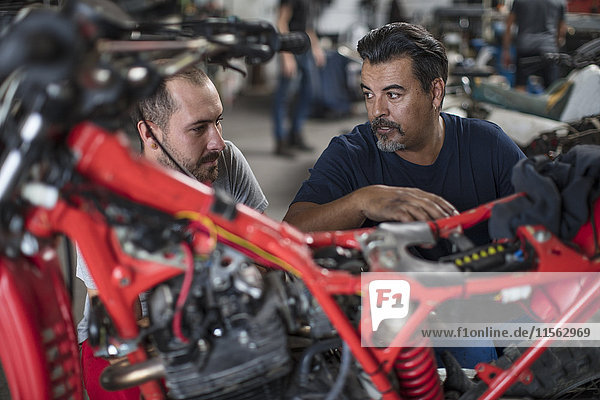 Two mechanics working on motorcycle in workshop together