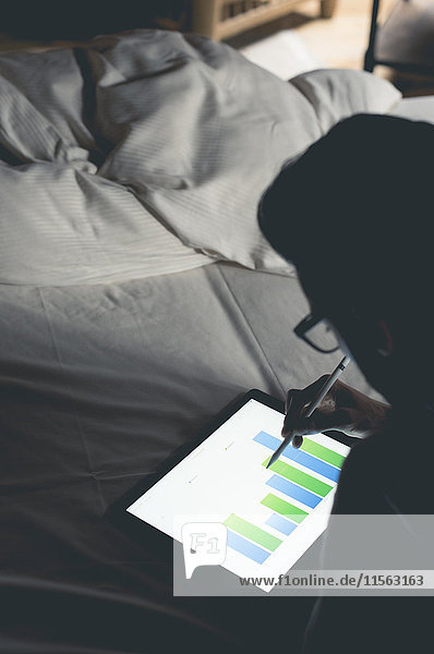 Junger Mann im Bett analysiert Daten auf Tablette