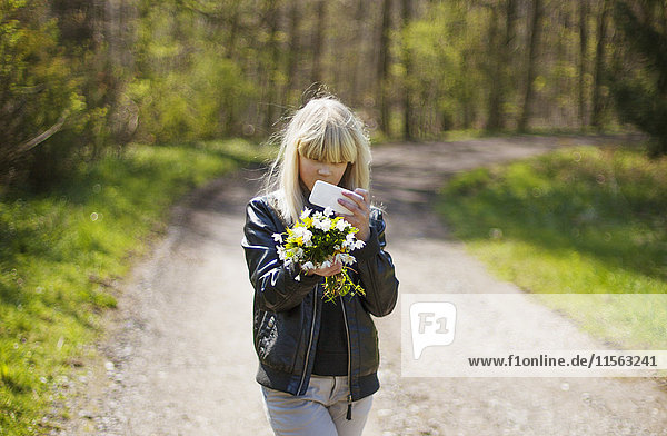 Denmark  Mon  Girl (14-15) using phone while walking and holding flowers