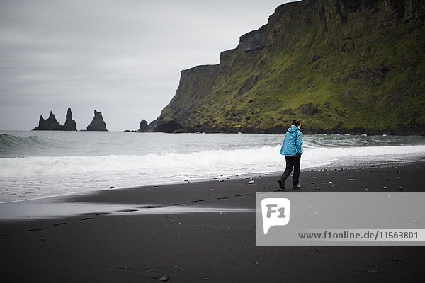 Island Sudurland Vik i Myrdal Wanderer am schwarzen Sandstrand zu Füßen der Klippe