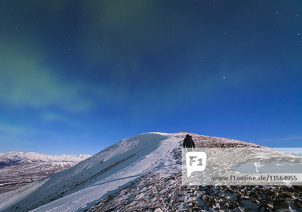 Ein Mann klettert in einer Mondnacht bei Minusgraden auf den Gipfel des Donnelly Dome (in der Nähe von Delta Junction)  um das Polarlicht zu fotografieren.