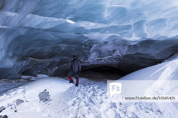 Ein Mann posiert vor einer Höhle am Ende des Felsgletschers (häufig falsch als Eel -Gletscher bezeichnet) in der Alaska Range im Winter; Alaska  Vereinigte Staaten von Amerika'.