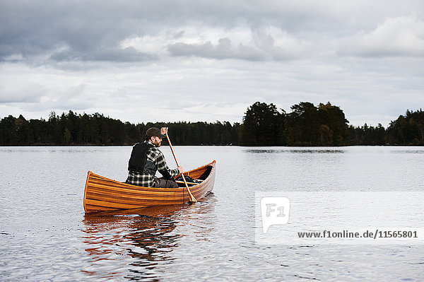 Schweden  Smaland  Reifer Mann im Boot auf dem See mit Wald am Horizont