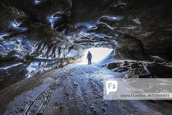 Ein Mann steht am Eingang eines langen Tunnels unter dem Eis des Castner-Gletschers in der Alaska Range; Alaska  Vereinigte Staaten von Amerika'.