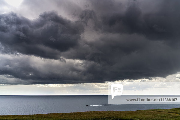 Bedrohliche dunkle Wolken über dem Meer und ein kleines Boot,  das die Küste entlang fährt; South Shields,  Tyne and Wear,  England'.